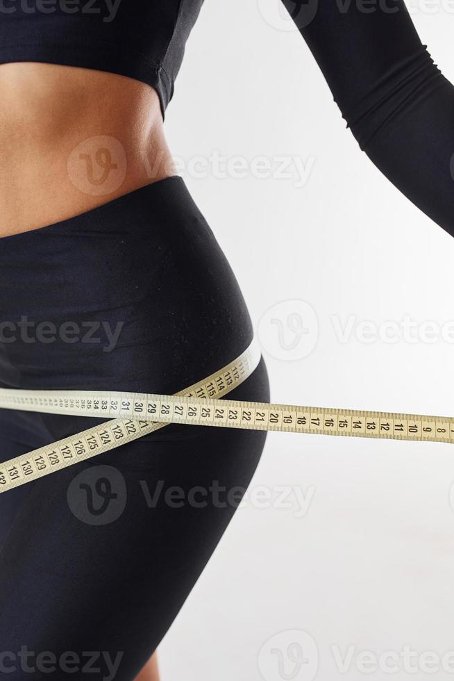 Close up view of sportive woman with measuring tape in the studio against white background photo