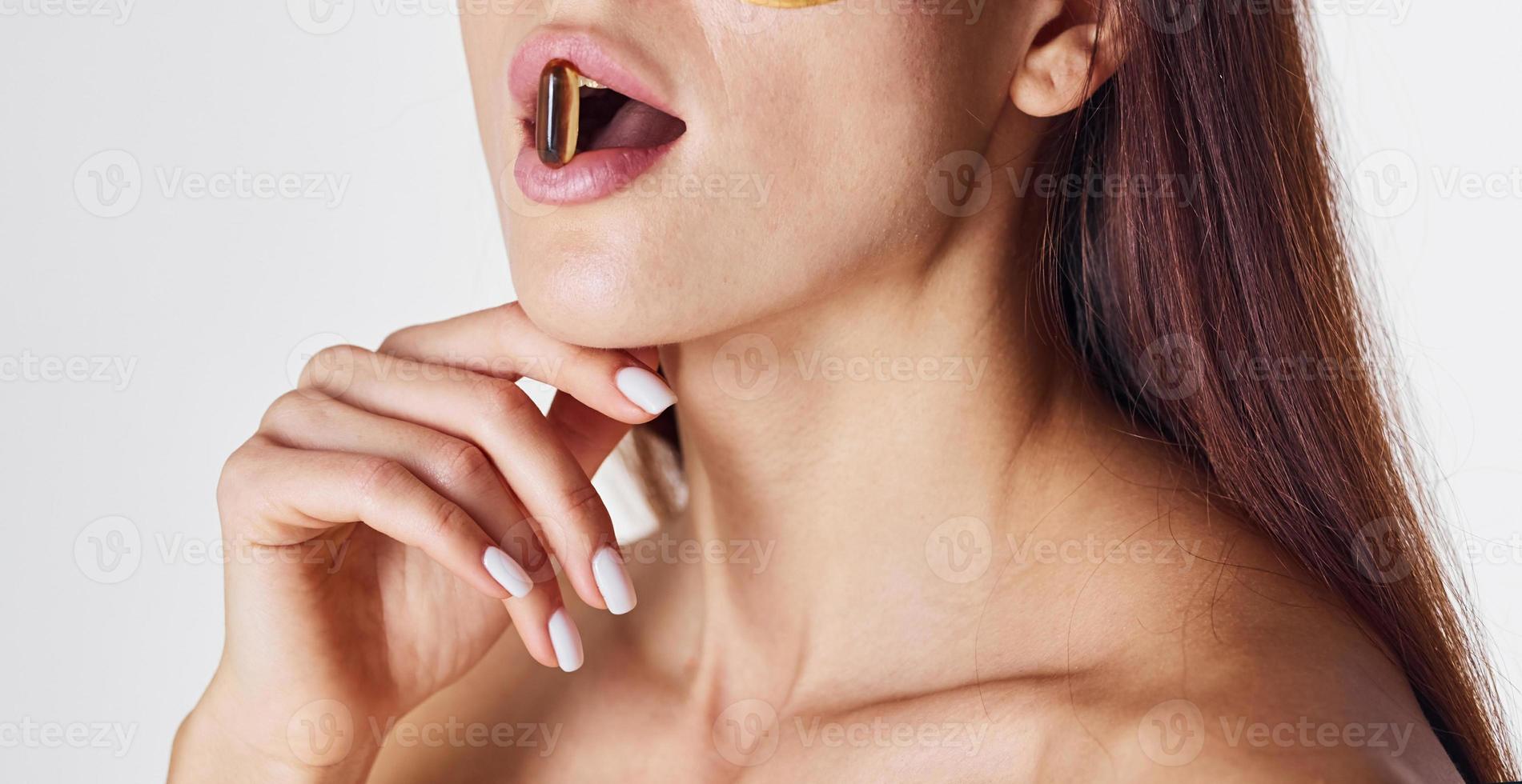 Naked woman in the studio against white background and with pill in mouth photo