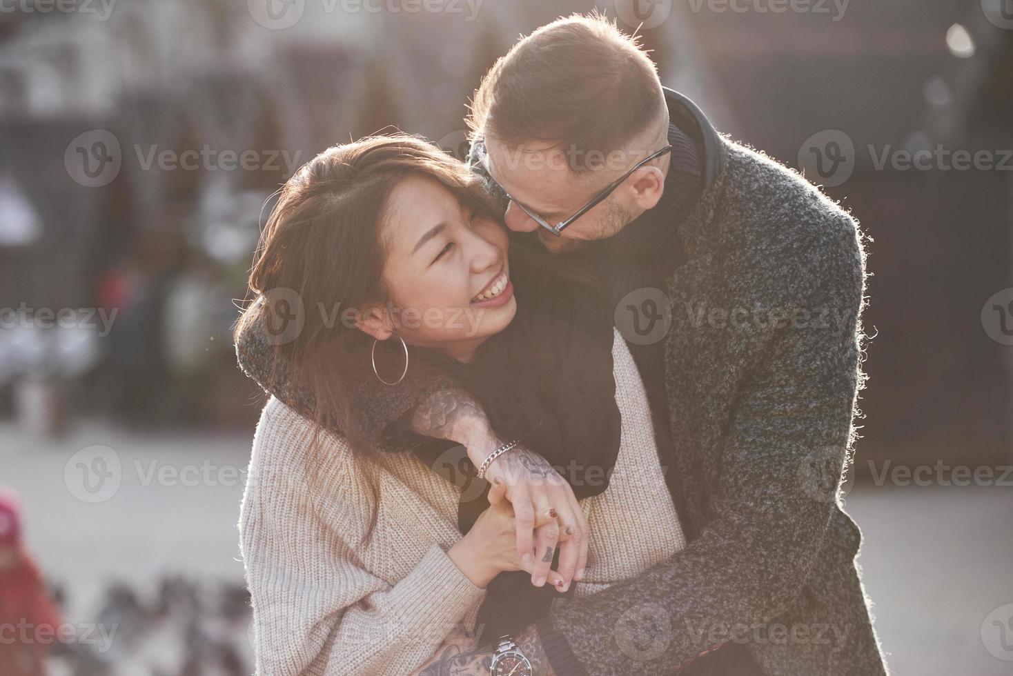 Cheerful multiracial couple embracing each other outdoors in the city. Asian girl with her caucasian boyfriend photo