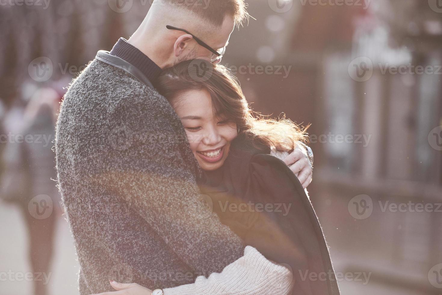 Cheerful multiracial couple embracing each other outdoors in the city. Asian girl with her caucasian boyfriend photo