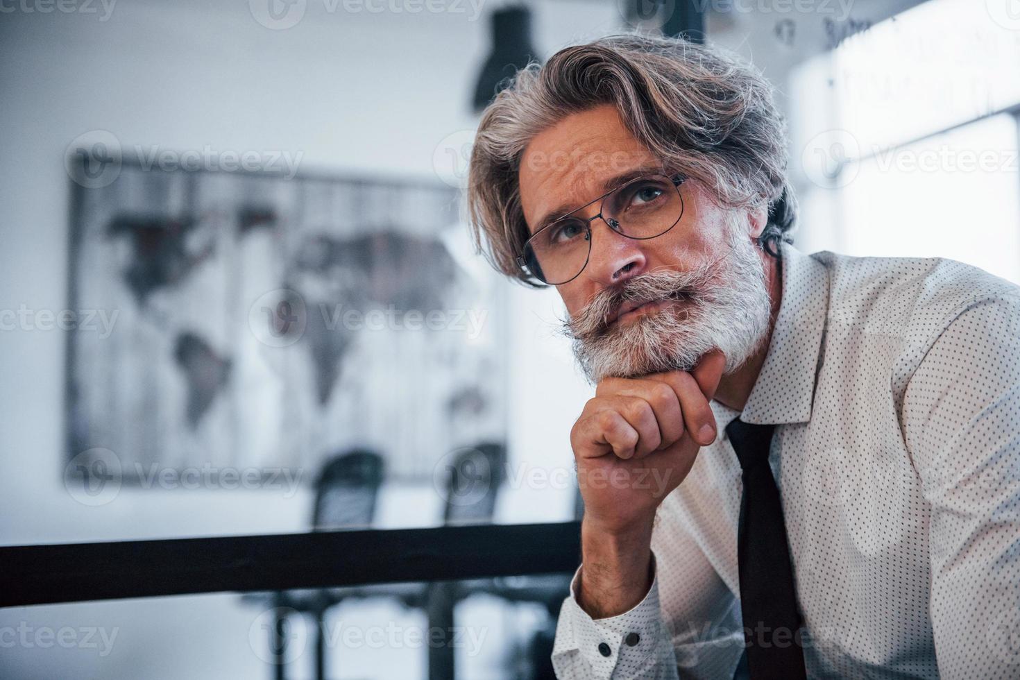 retrato de hombre de negocios maduro con cabello gris y barba en ropa formal que se sienta en la oficina foto