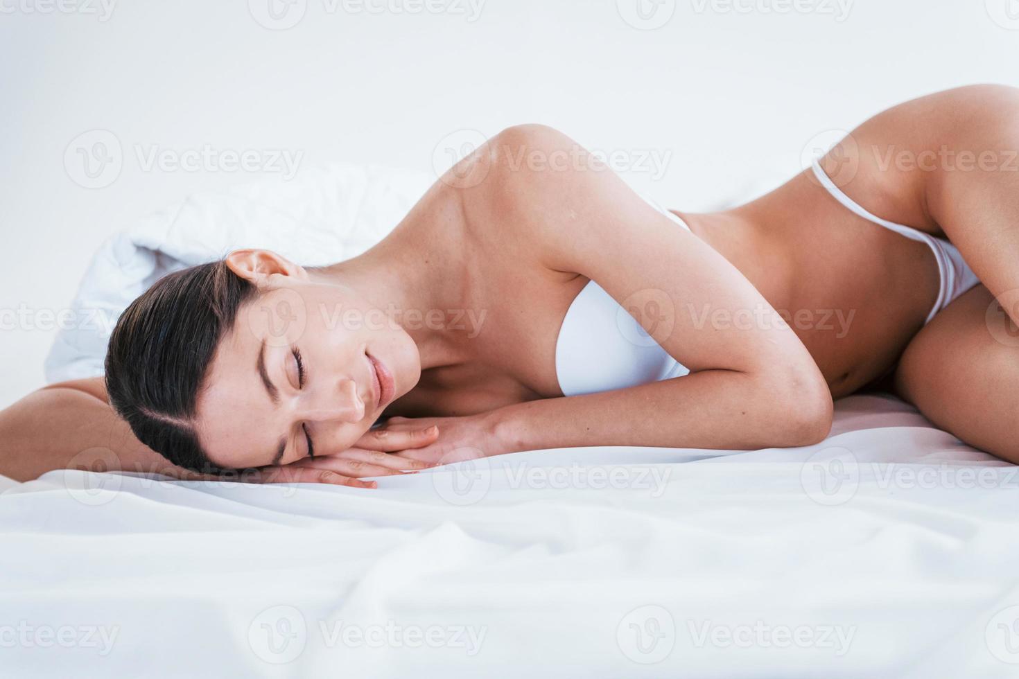 Young woman in underwear and with nice body shape lying down in the studio against white background photo