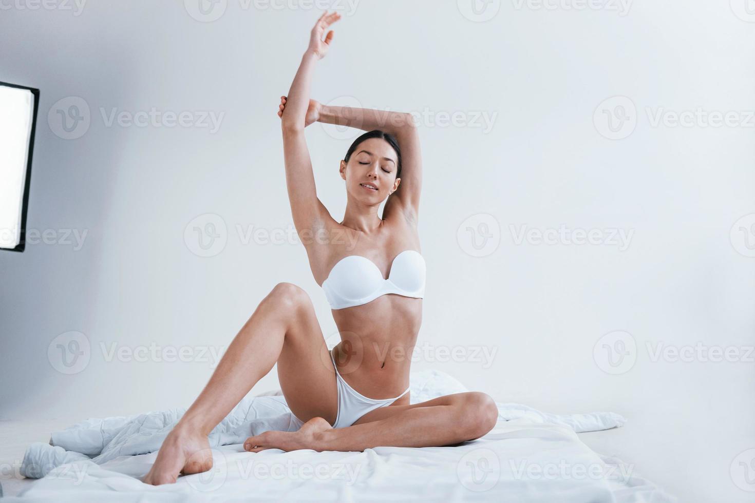 Young woman in underwear and with nice body shape sits in the studio against white background photo