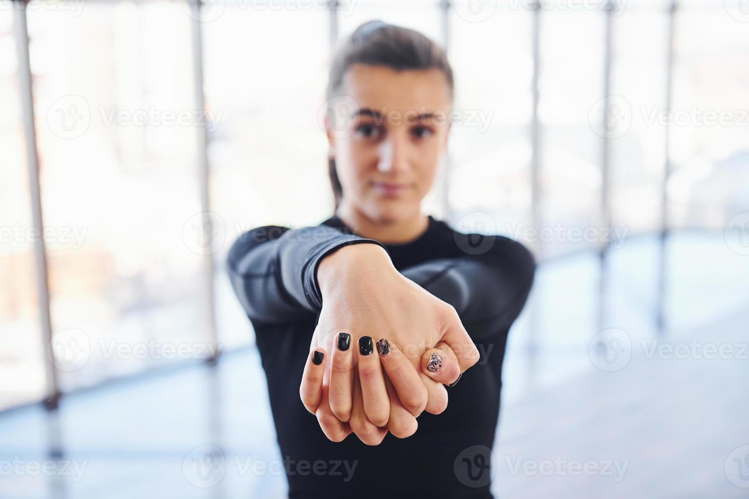 Confident young sporty woman in sportswear doing warm up exercises for hands against window photo