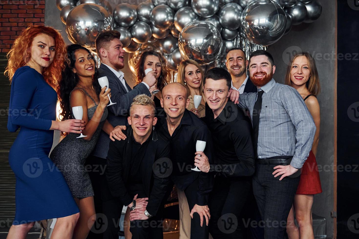 People in elegant clothes with drinks in hands standing together and celebrating New Year holidays in christmas decorated room photo