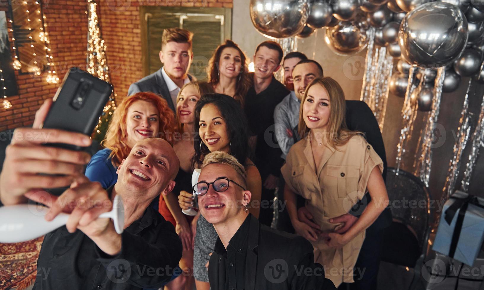 Man taking selfie of his friends that standing in christmas decorated room and celebrating New Year holidays photo