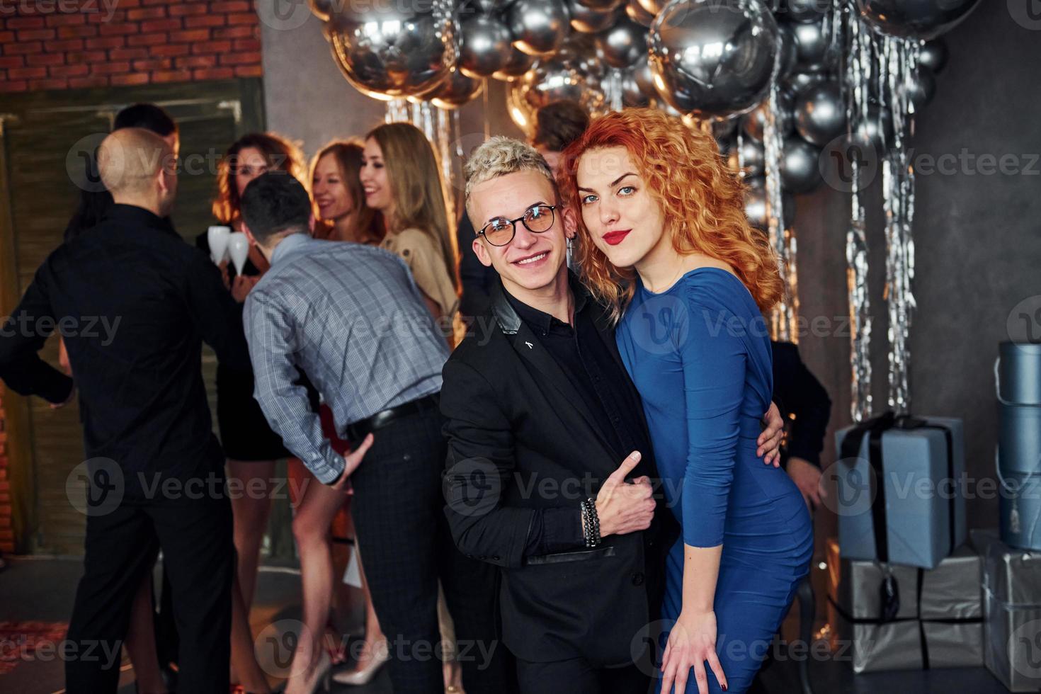 Young man with redhead woman is together against their friends in christmas decorated room and celebrating New Year photo