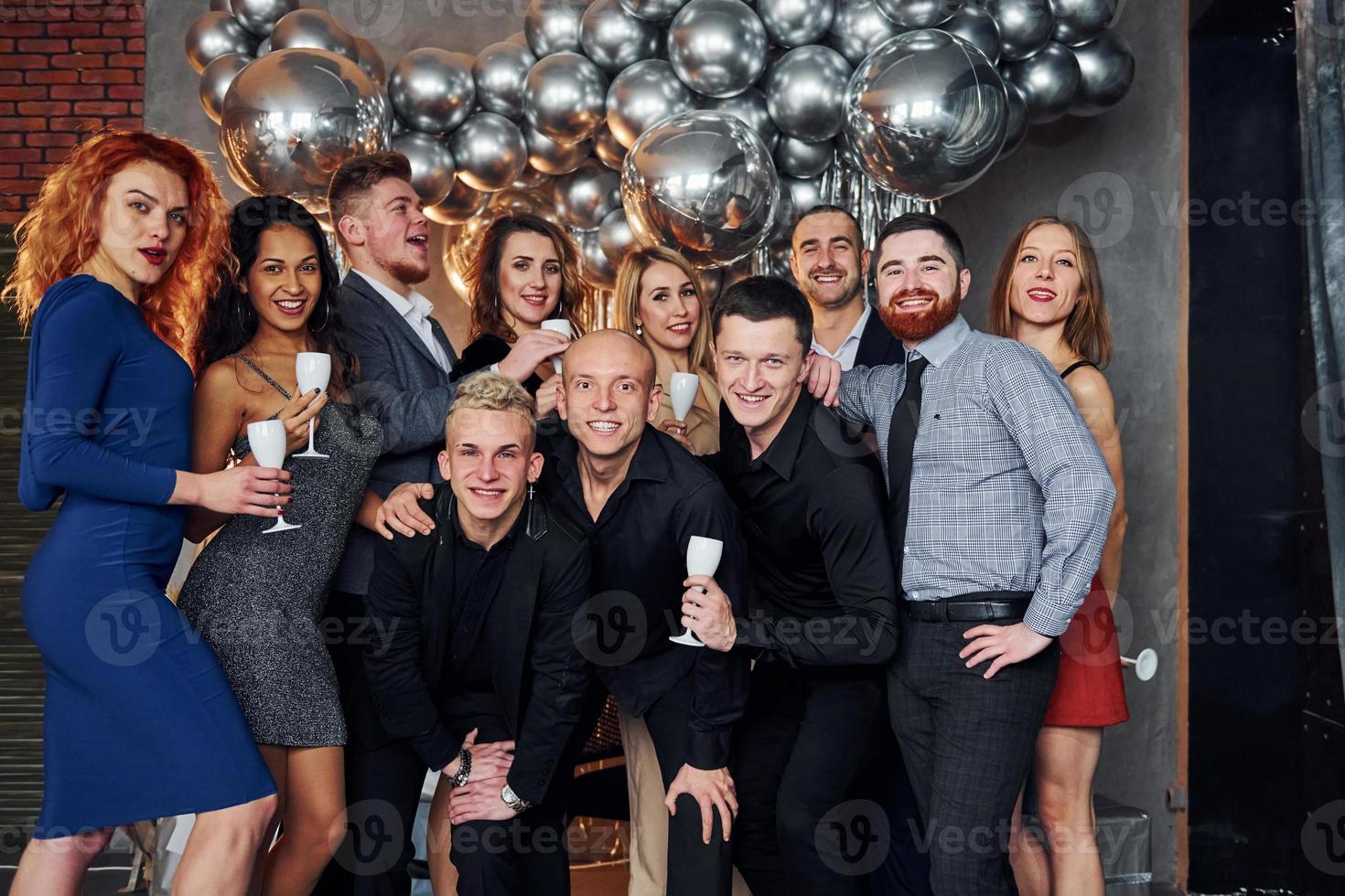 People in elegant clothes with drinks in hands standing together and celebrating New Year holidays in christmas decorated room photo