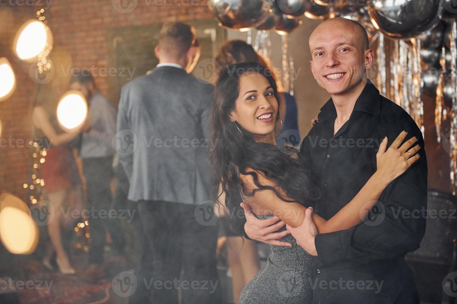 Young couple standing together against their friends in christmas decorated room and celebrating New Year photo