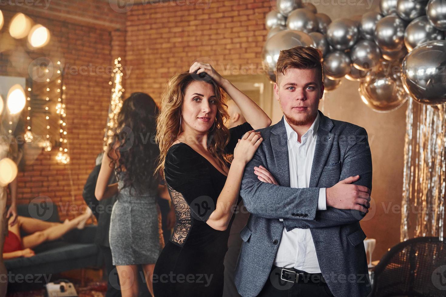 Young couple standing together against their friends in christmas decorated room and celebrating New Year photo