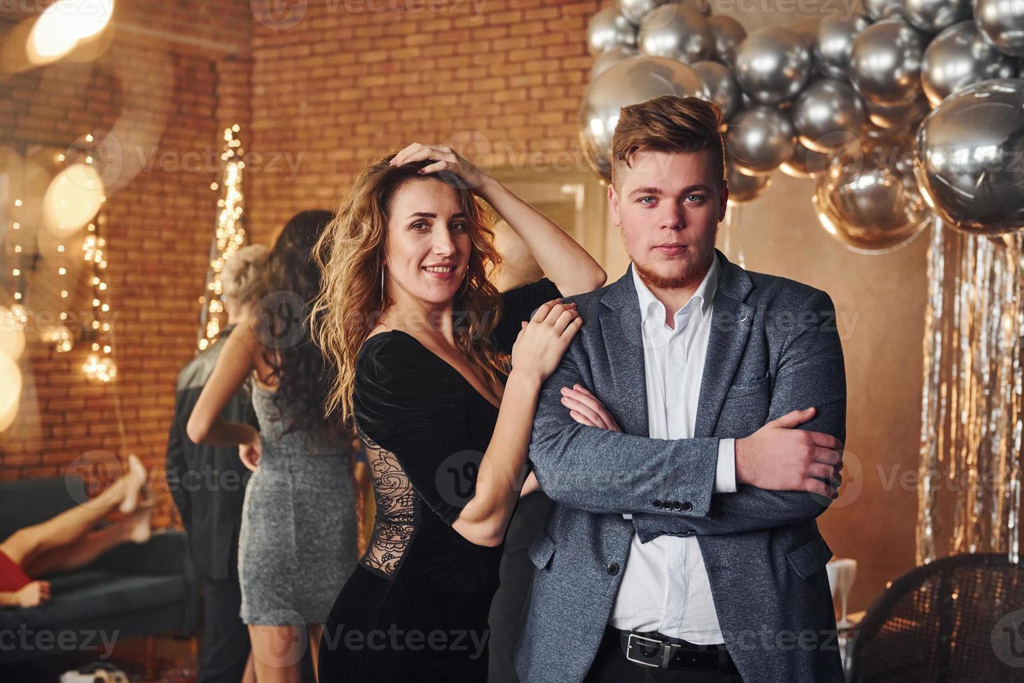 Young couple standing together against their friends in christmas decorated room and celebrating New Year photo