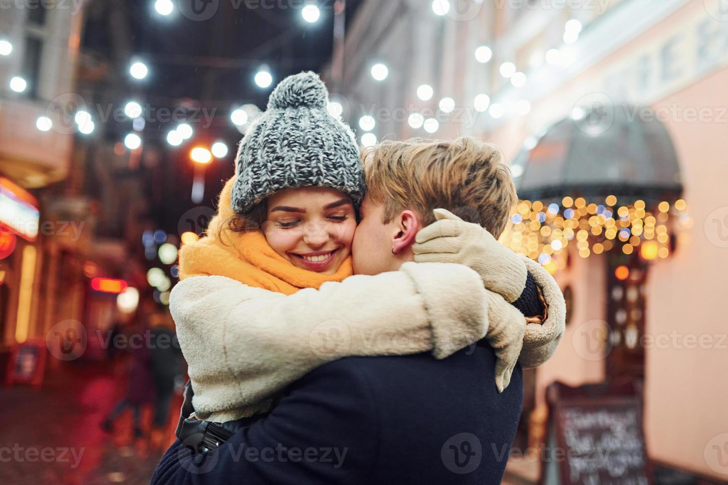 Positive young couple in warm clothes embracing each other on christmas decorated street photo