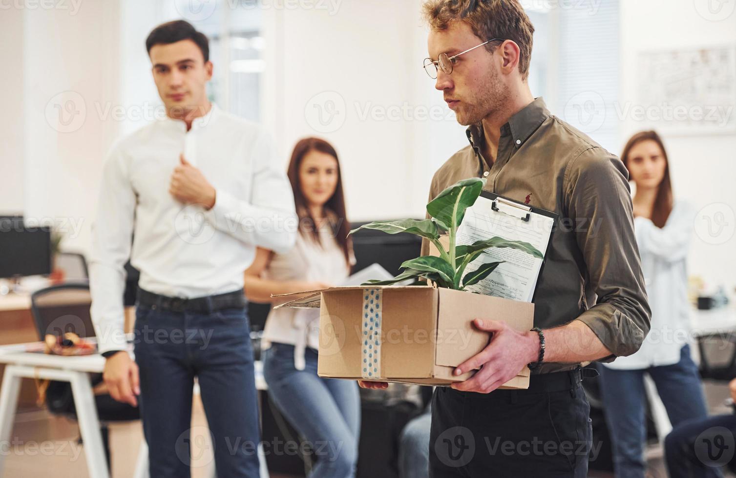 Man in glasses with box is in front of business people that working together in the modern office photo