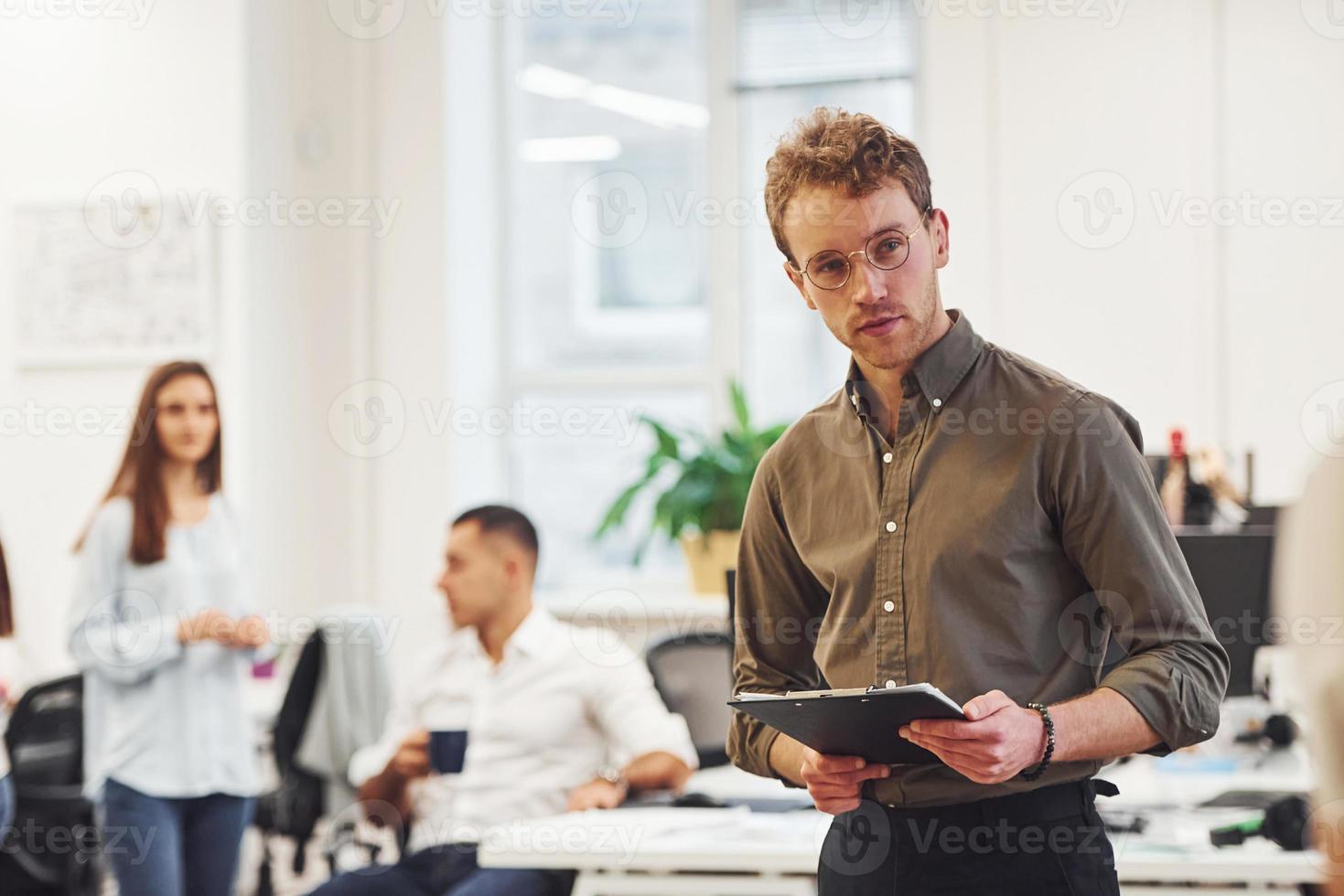 Man in glasses standing in front of business people that working together in the modern office photo