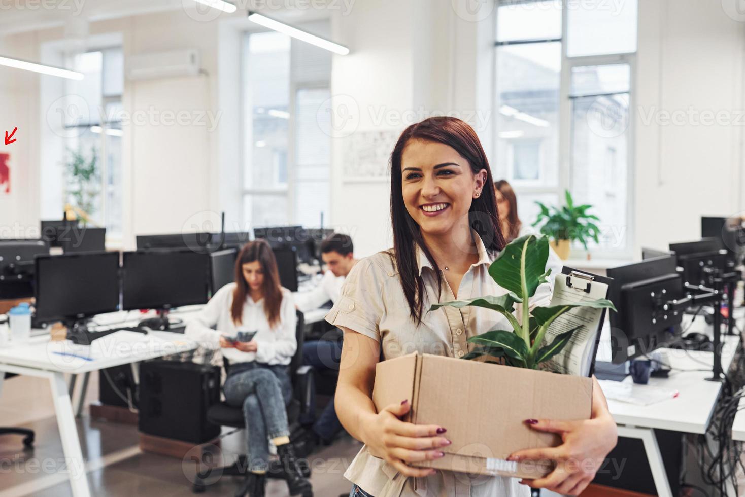 Smiling woman with box is in front of business people that working together in the modern office photo