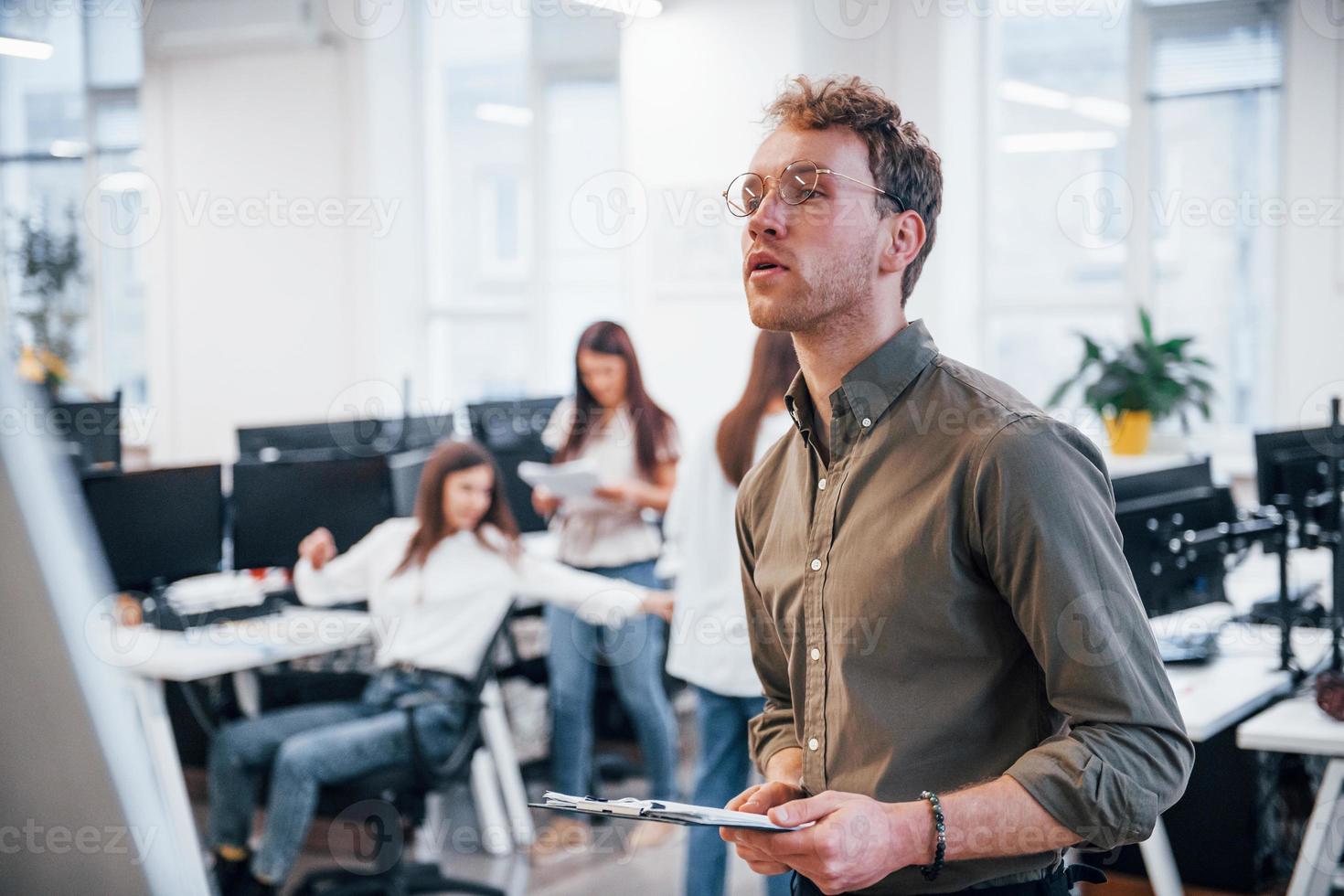 Man in glasses standing in front of his colleagues in the office photo