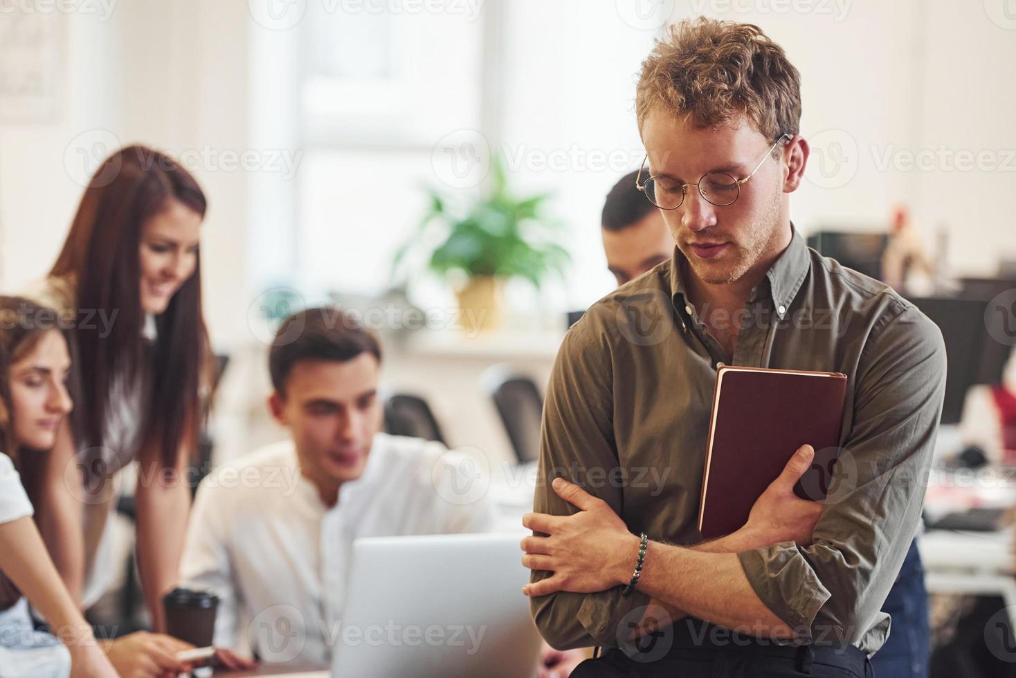 Man in glasses standing in front of his colleagues in the office photo