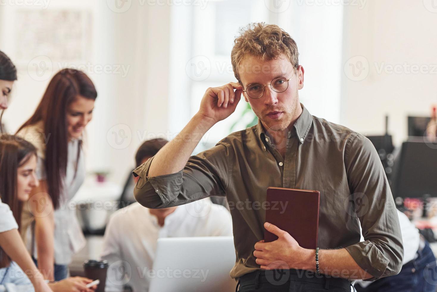 Man in glasses standing in front of his colleagues in the office photo