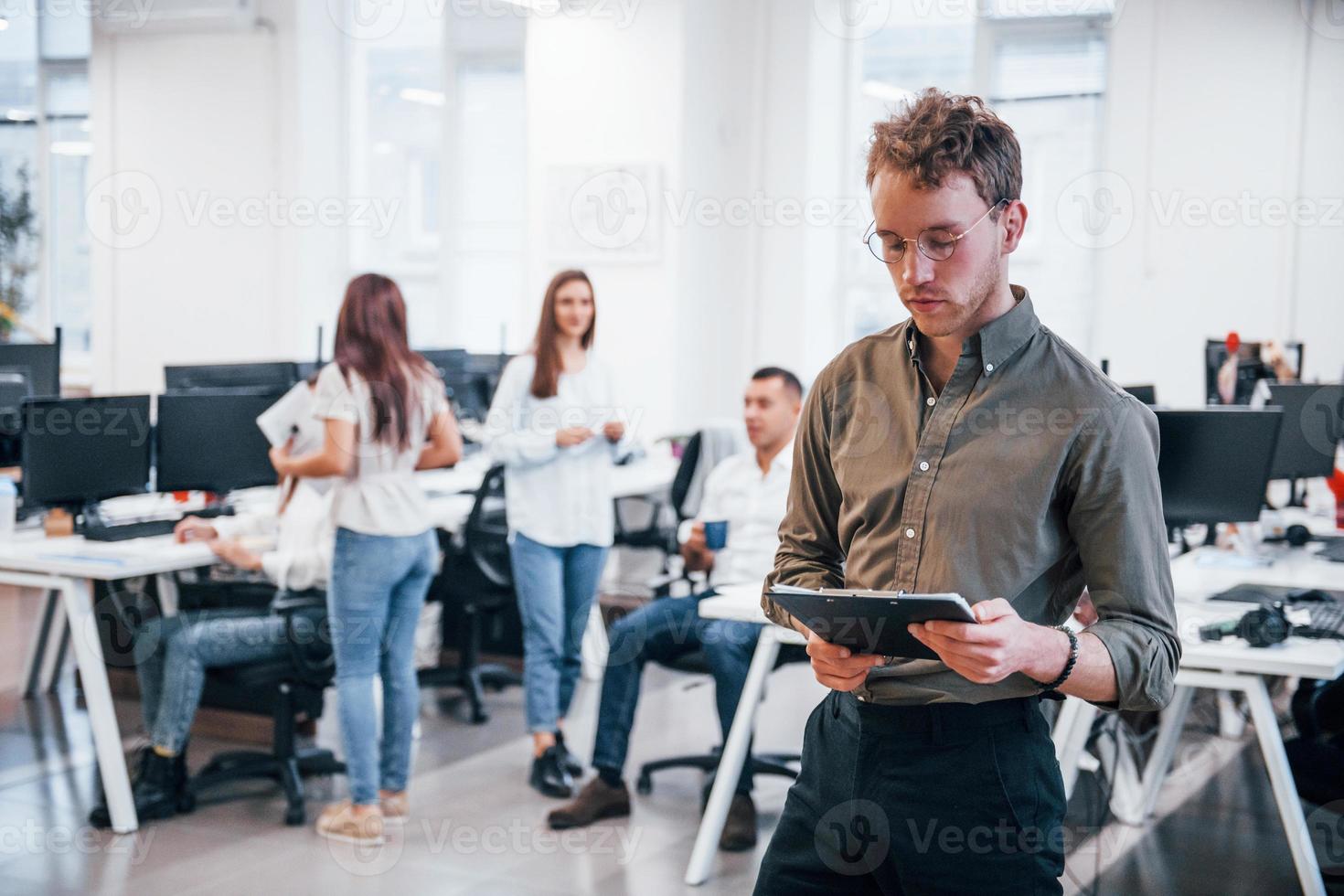 Man in glasses standing in front of his colleagues in the office photo