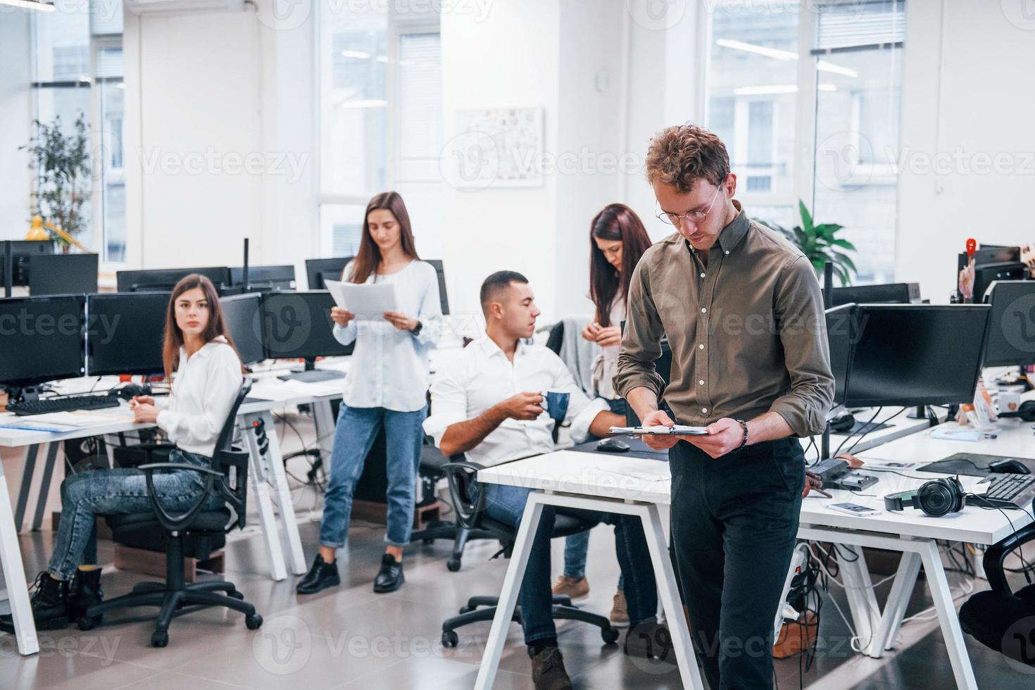 Man in glasses standing in front of his colleagues in the office photo
