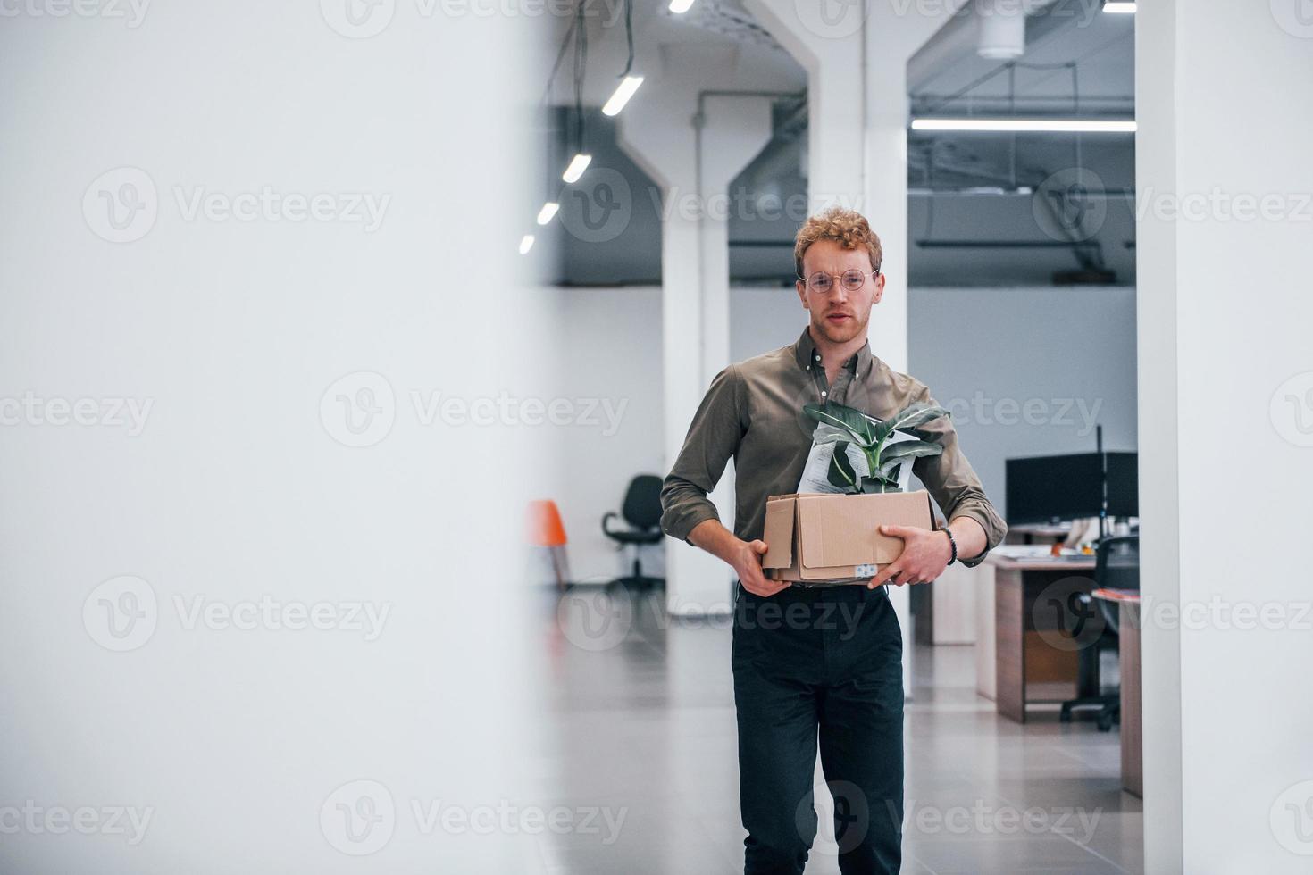 Office worker in formal wear walking with box with green plant inside of it photo