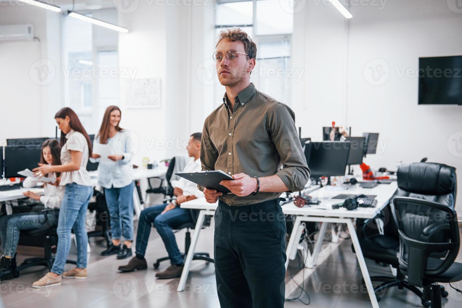 Man in glasses standing in front of his colleagues in the office photo