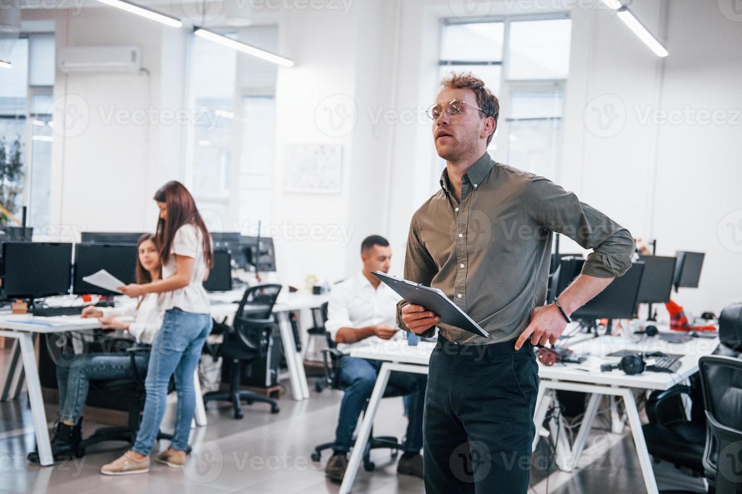 Man in glasses standing in front of his colleagues in the office photo