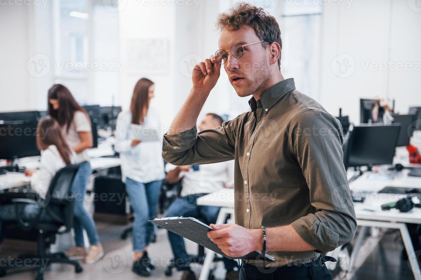 Man in glasses standing in front of his colleagues in the office photo