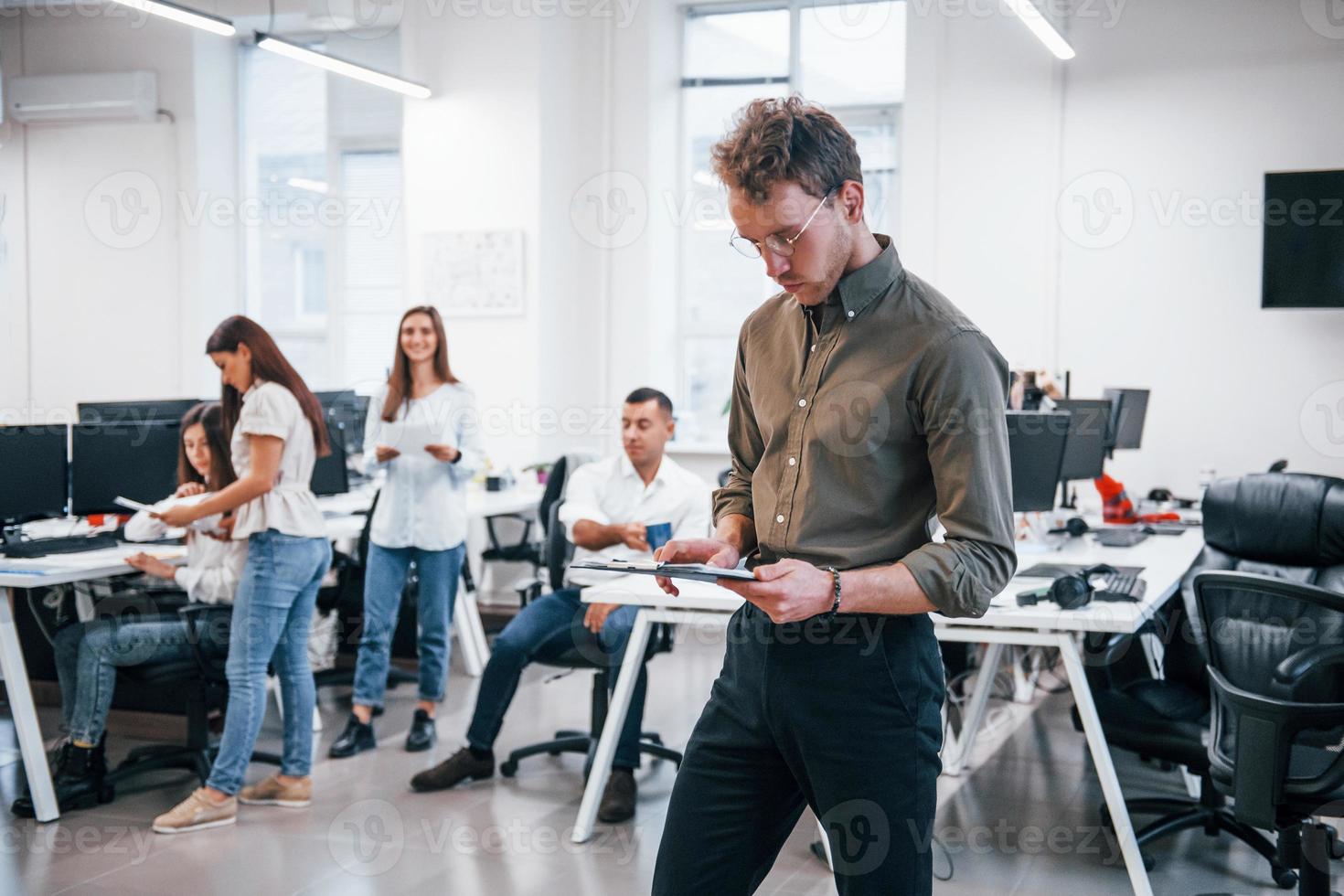 Man in glasses standing in front of his colleagues in the office photo
