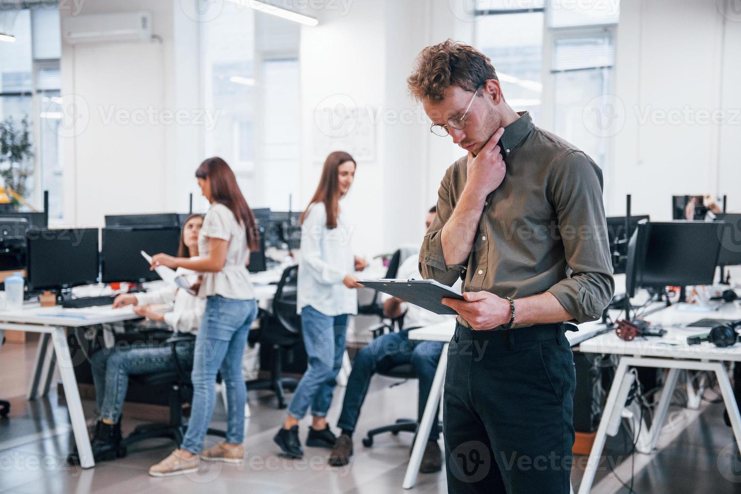 Man in glasses standing in front of his colleagues in the office photo