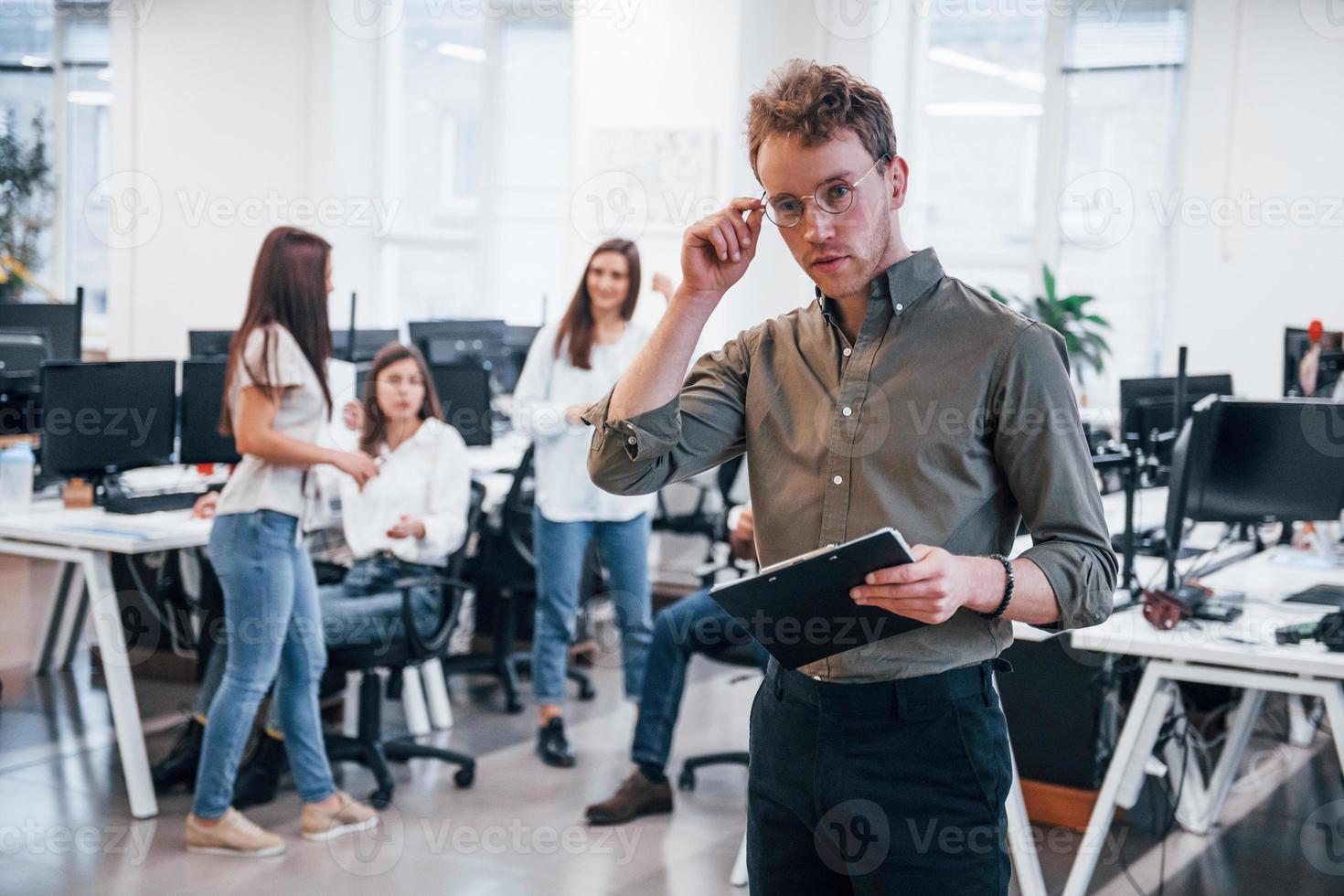 Man in glasses standing in front of his colleagues in the office photo