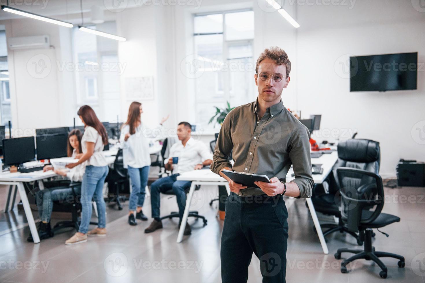 Man in glasses standing in front of his colleagues in the office photo