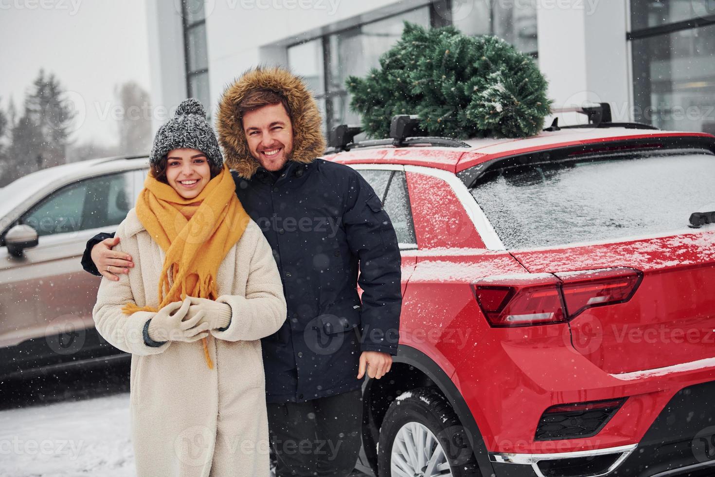 Young couple standing near car with tree on the top. Together outdoors at winter time photo