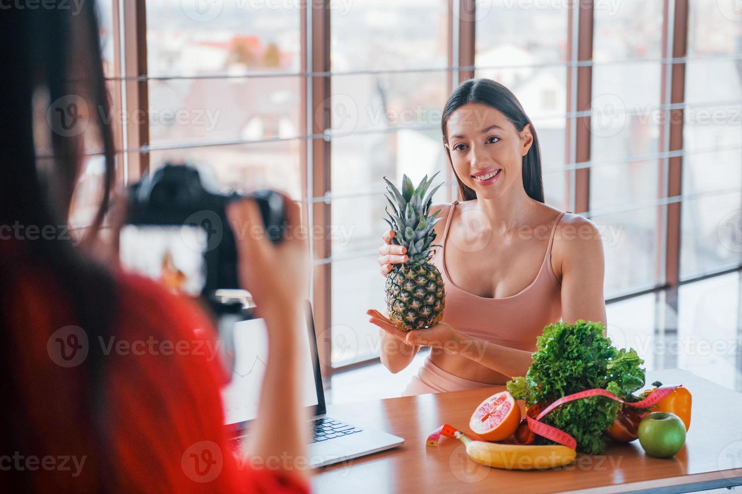 Fitness model have photoshoot by female photographer indoors by the table with healthy food photo