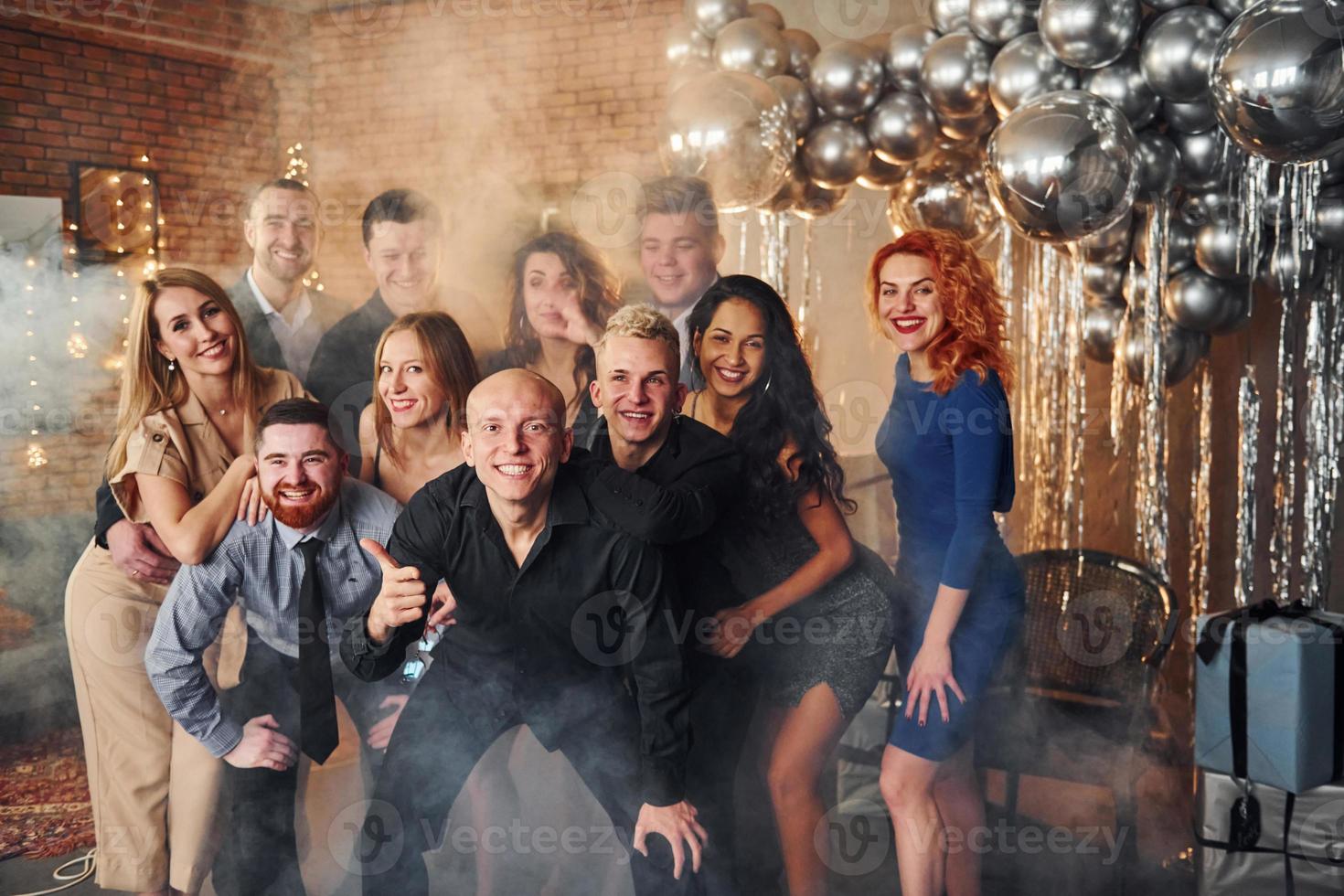 Smiling group of young people have fun indoors of christmas decorated room. Celebrating New Year holidays photo