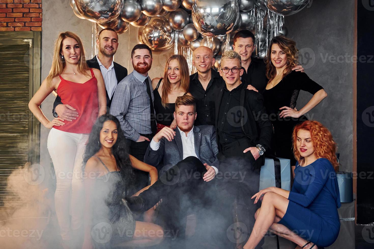 mujeres y hombres jóvenes vestidos de fiesta celebrando el año nuevo juntos en el interior de una habitación decorada con navidad foto