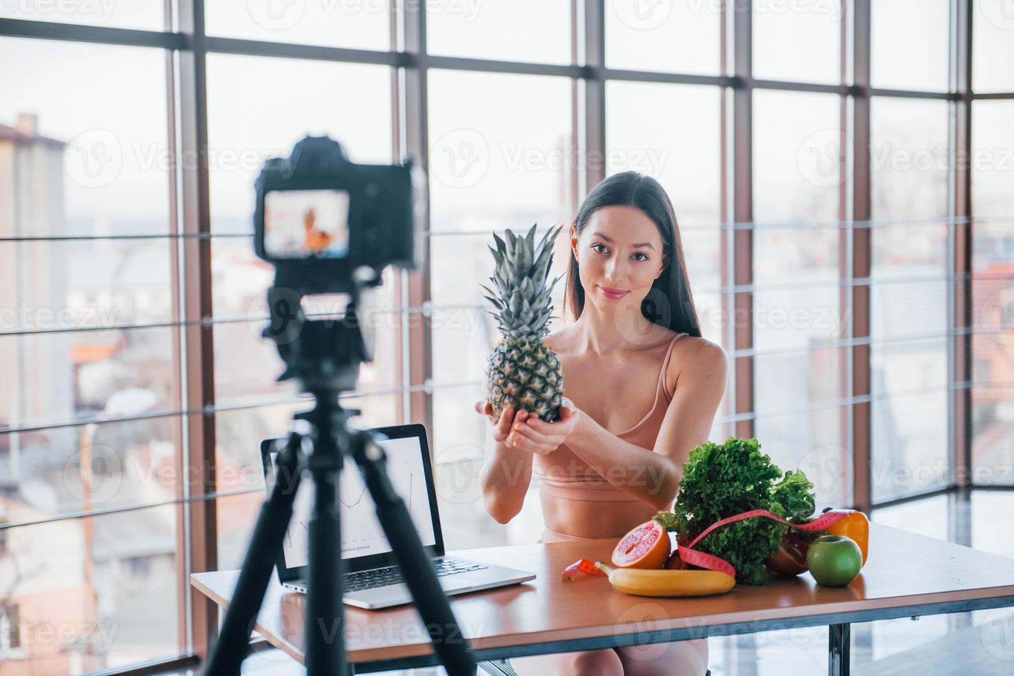 Young fitness vlogger doing video indoors by sitting near table with healthy food photo