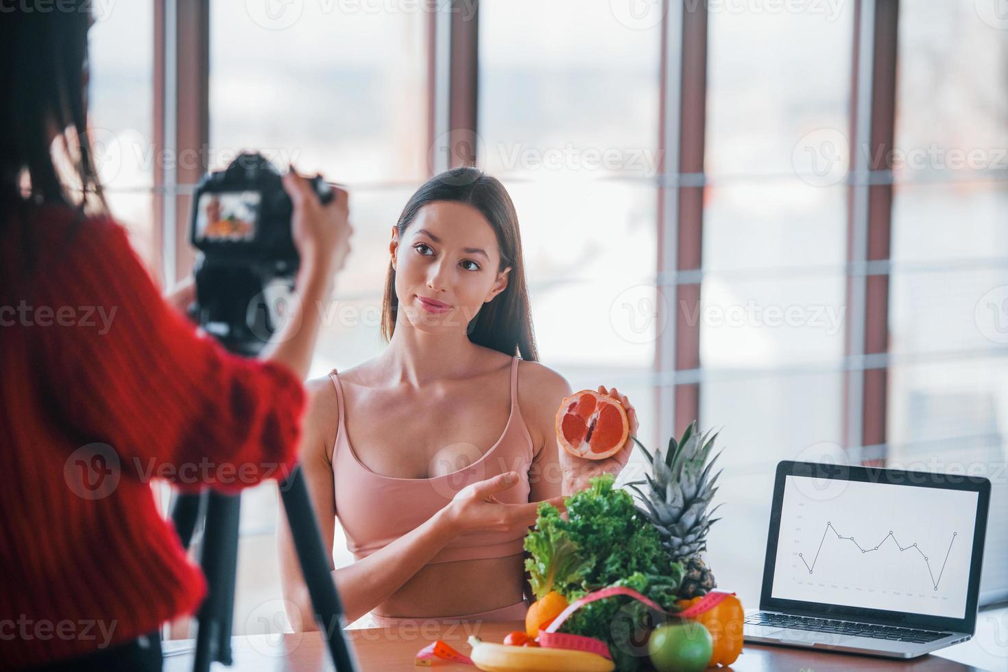 Fitness model have photoshoot by female photographer indoors by the table with healthy food photo