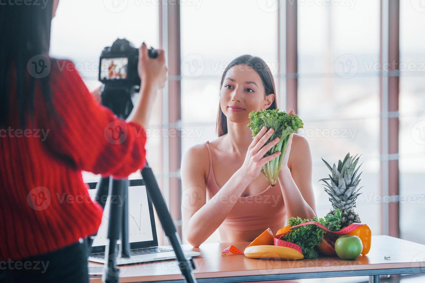 Fitness model have photoshoot by female photographer indoors by the table with healthy food photo