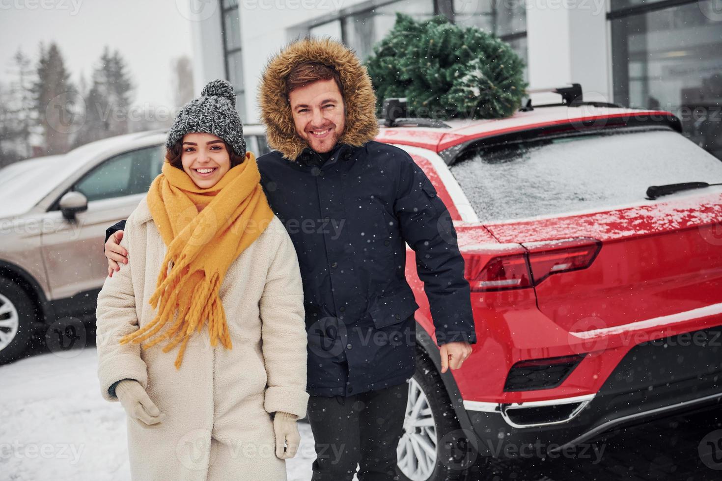 Young couple standing near car with tree on the top. Together outdoors at winter time photo