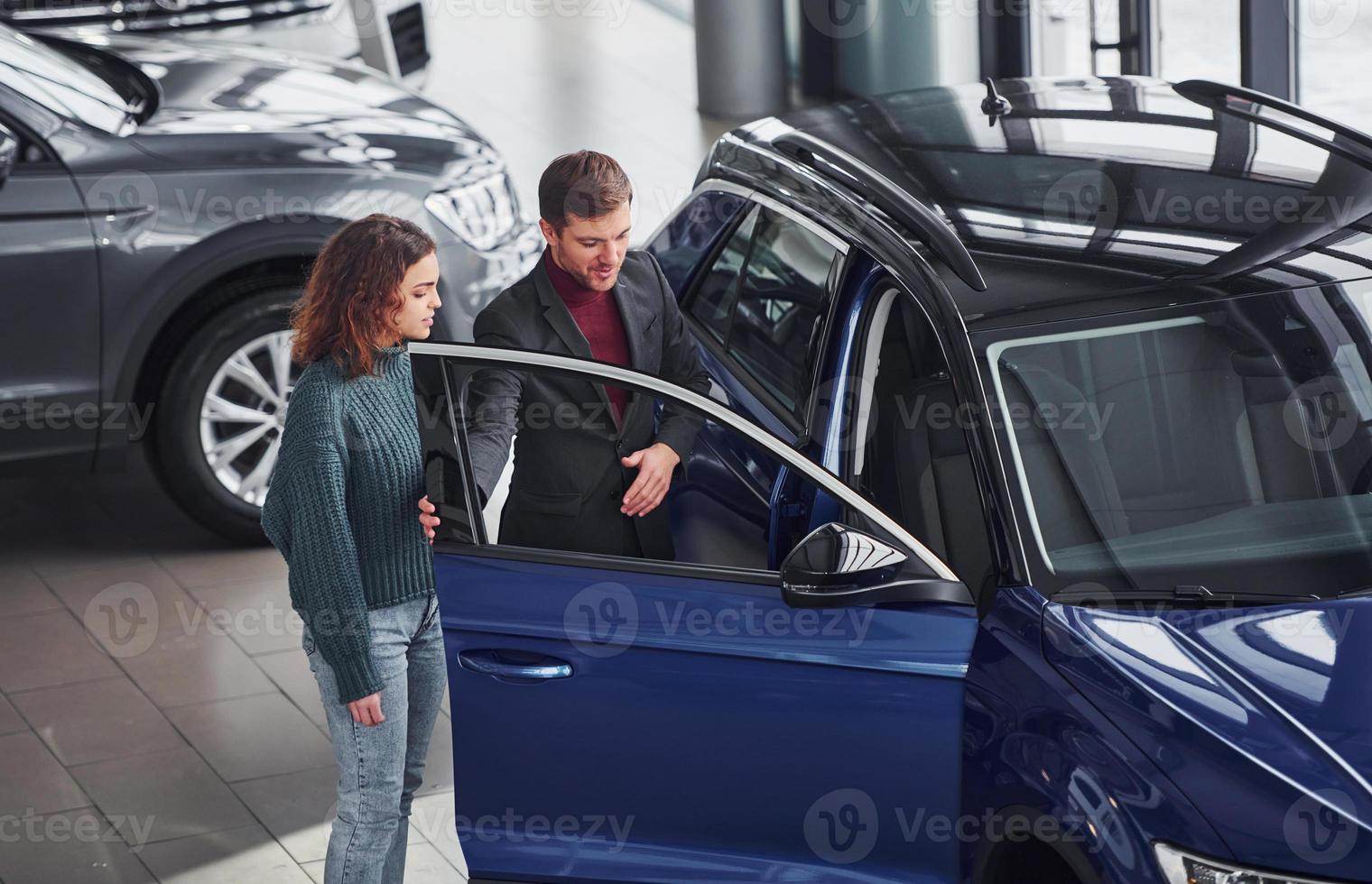 Professional salesman assisting young girl by choosing new modern automobile indoors photo