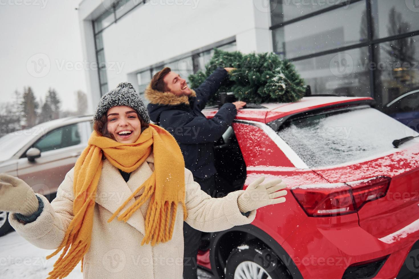 Young couple standing near car with tree on the top. Together outdoors at winter time photo