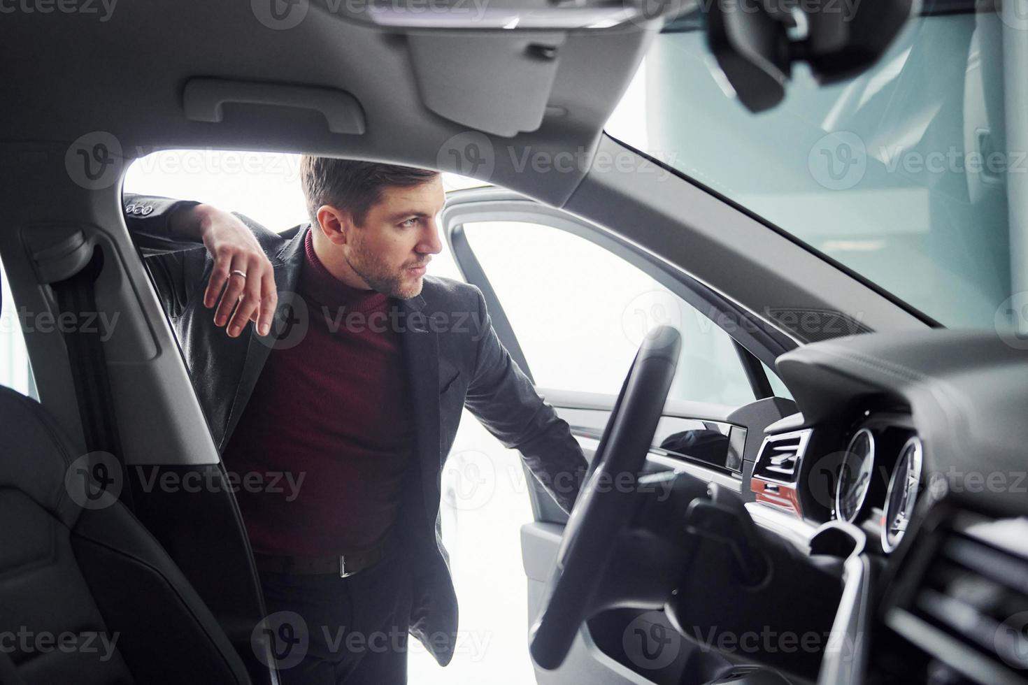 Young business man in luxury suit and formal clothes is indoors near the car photo