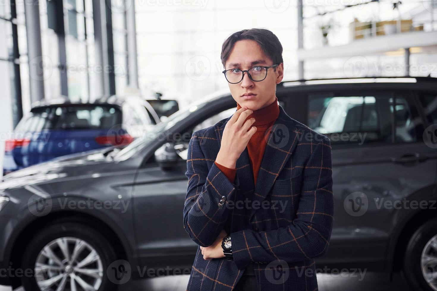 Posing for the camera. Young business man in luxury suit and formal clothes is indoors near the car photo