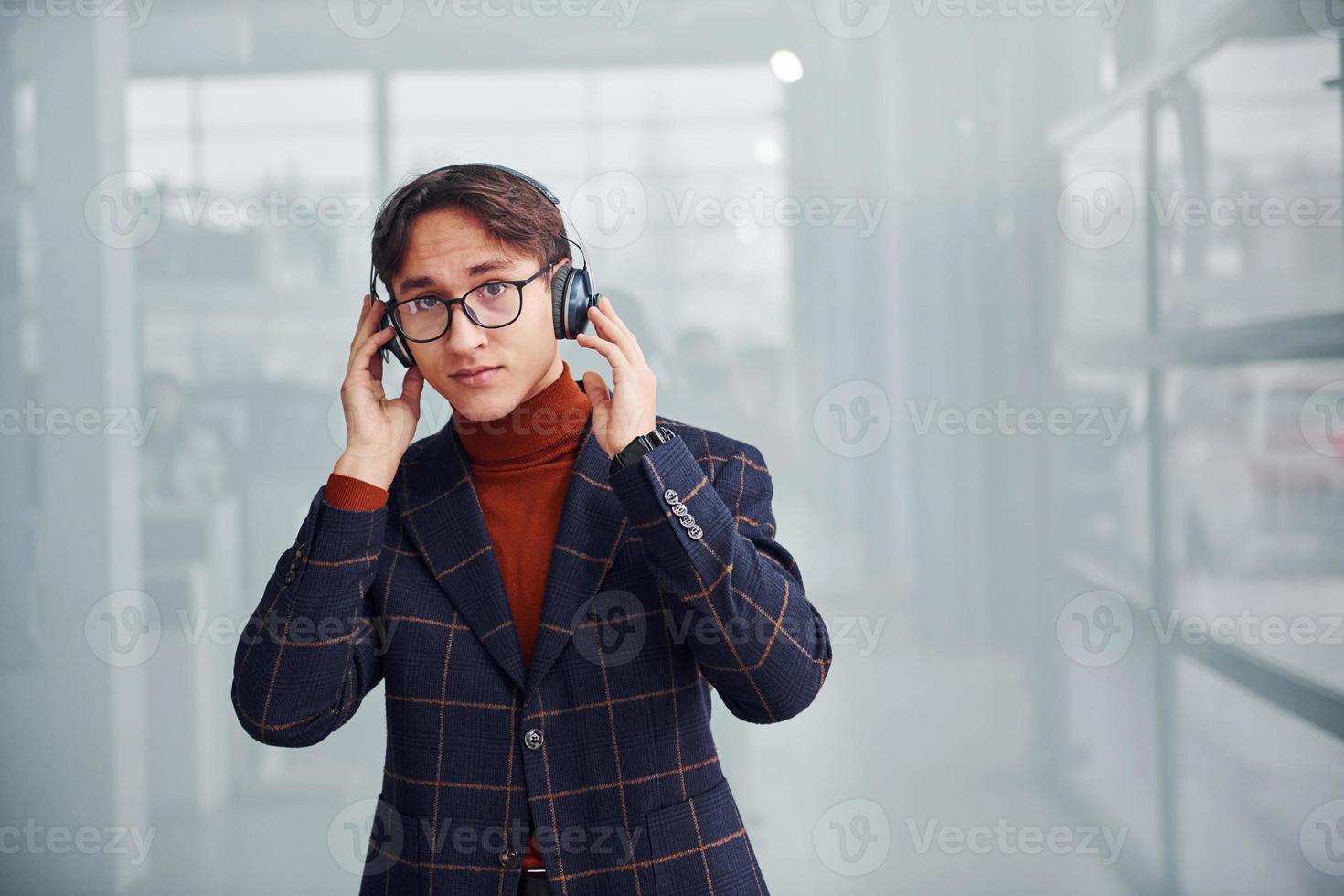 escuchando la música en los auriculares. un joven hombre de negocios con traje de lujo y ropa formal está en el interior de la oficina foto