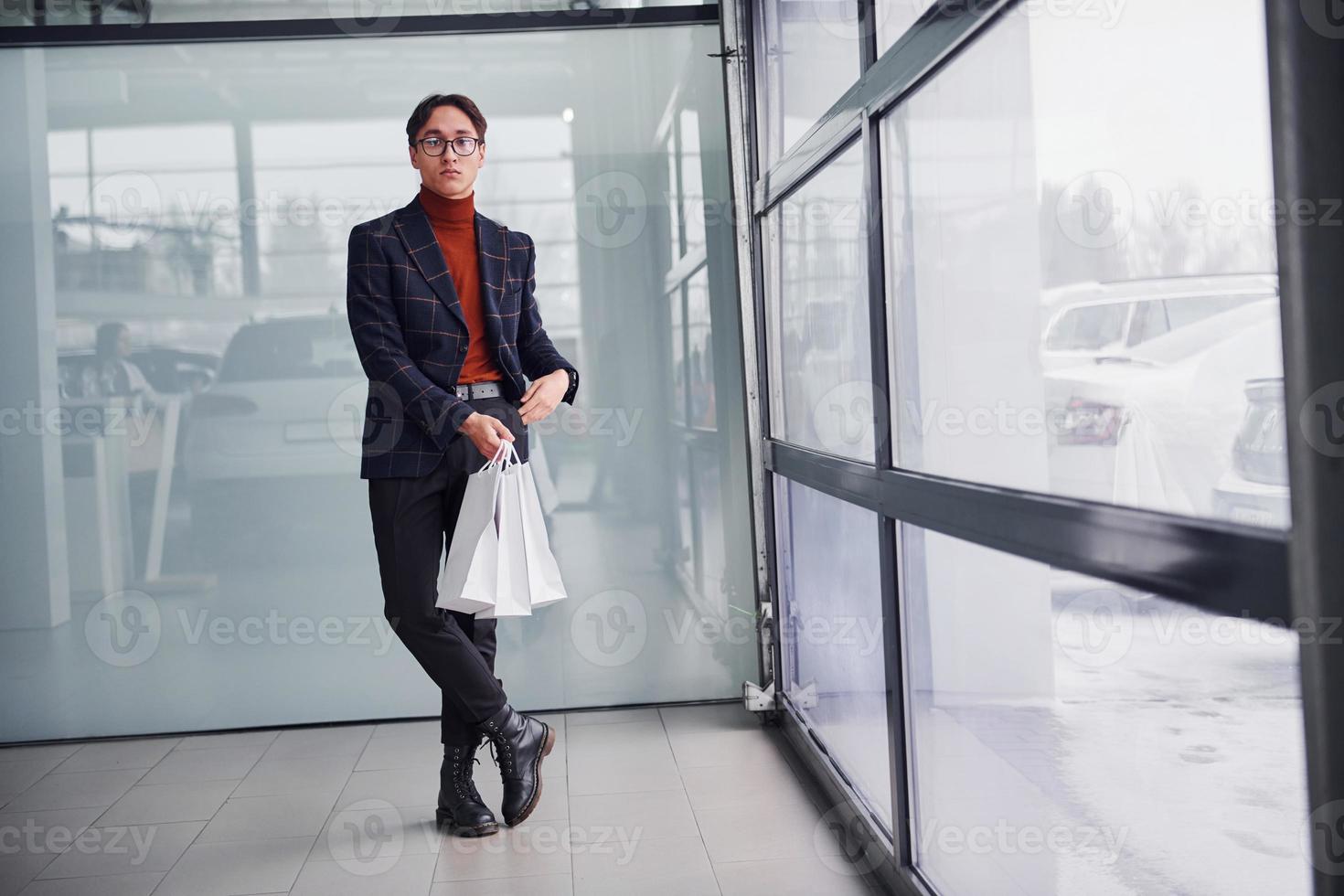 With shopping bags. Young business man in luxury suit and formal clothes is indoors in the office photo