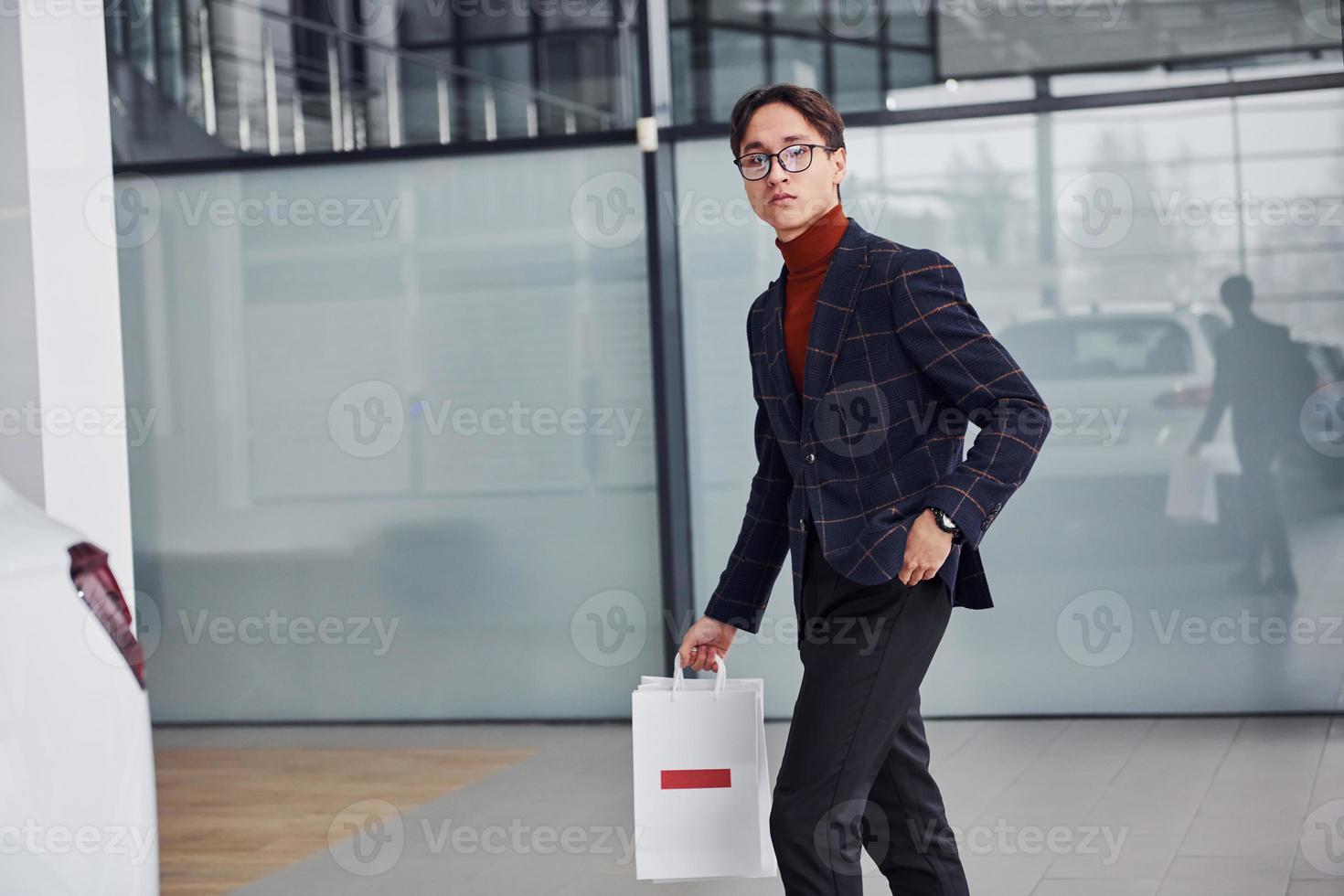 With shopping bags. Young business man in luxury suit and formal clothes is indoors in the office photo