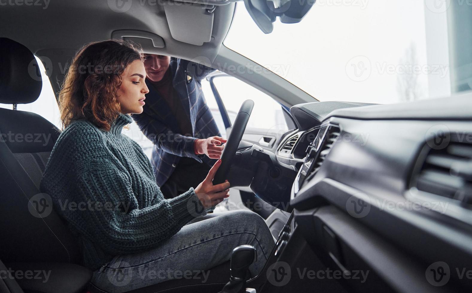 Professional salesman assisting young girl by choosing new modern automobile indoors. Woman sitting inside photo