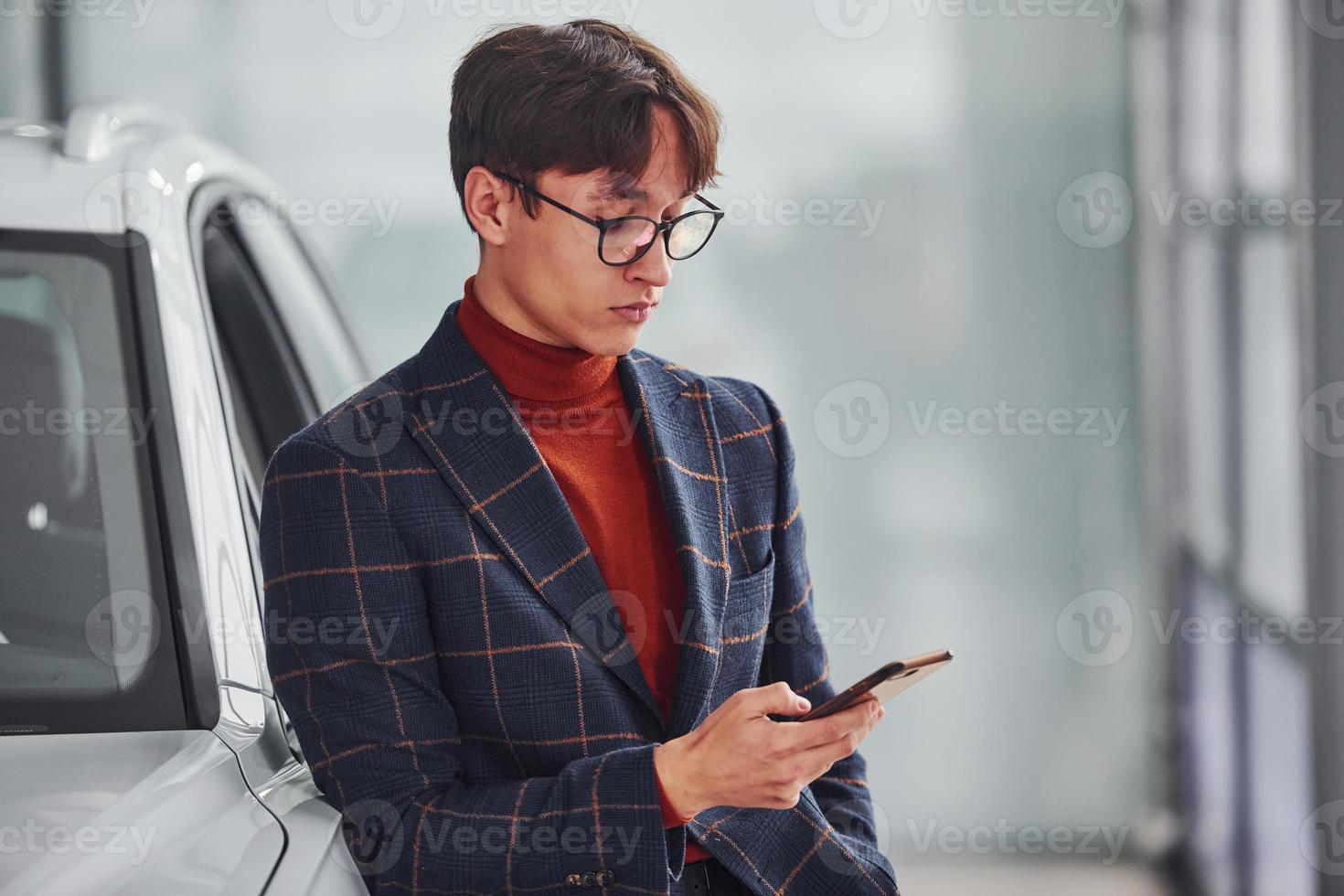 Hipster in formal wear and in eyewear standing near white modern car indoors photo