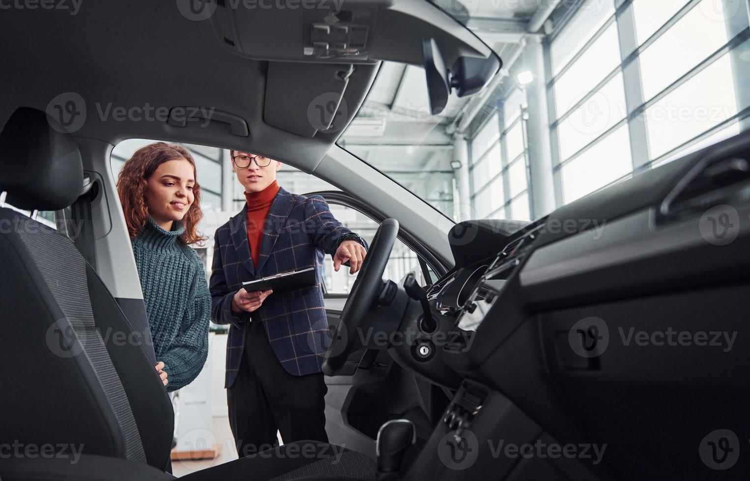 Professional salesman assisting young girl by choosing new modern automobile indoors. Woman sitting inside photo